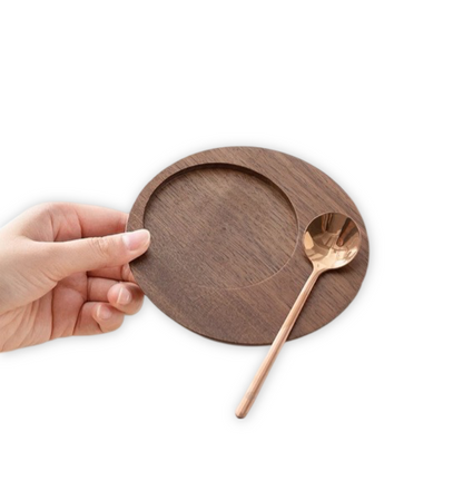 Wooden coffee cup saucer with gold spoon, held by a hand.