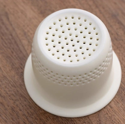 White ceramic tea strainer from the "Dongli" Portable Tea Set on a wooden surface.