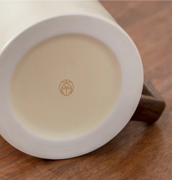 Bottom view of the "Half Sight" Coffee Cup by Mr. Nanshan, featuring an elegant insignia on its base, on a wooden table.